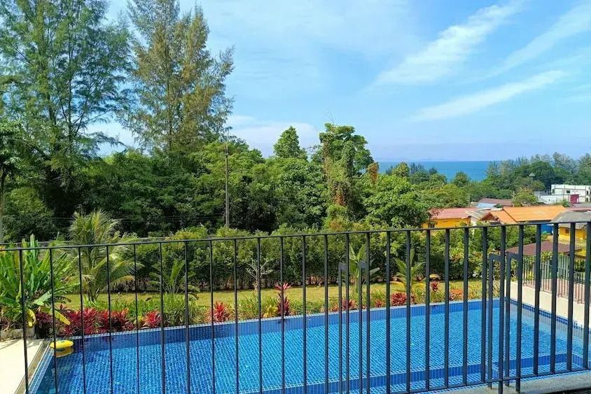 Blick von einem Balkon auf einen Pool und üppige tropische Vegetation mit Meereshorizont
