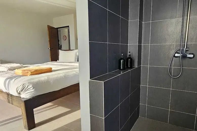 Modernes Badezimmer mit dunkler Fliesenverkleidung und Blick auf das Schlafzimmer