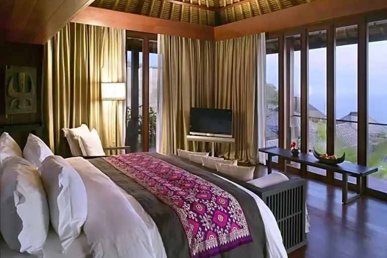 Schlafzimmer einer luxuriösen Villa mit Doppelbett, balinesischer Holzdecke und Panoramablick auf den Ozean.
