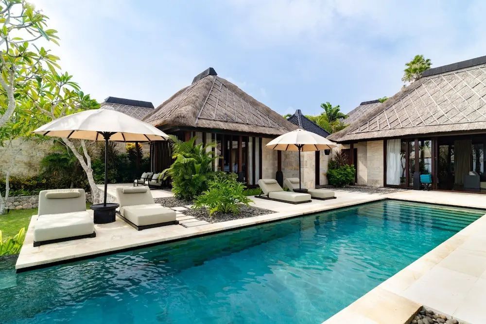 Private Terrasse der Premier Villa mit Infinity Pool, Sonnenliegen und traditionellen Reetdach Pavillons.
