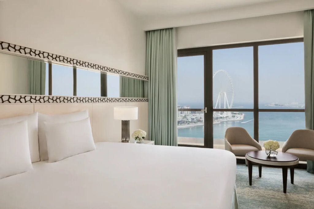 Zimmer mit Doppelbett und großer Fensterfront mit Meer- und Riesenradblick.