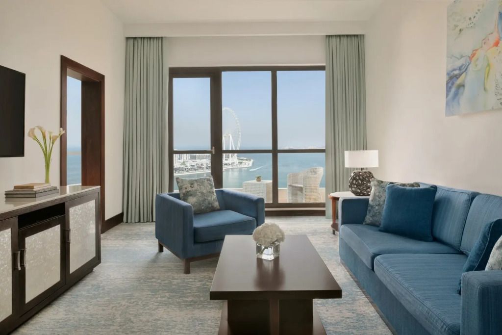 Wohnbereich mit blauen Sofas und Glastüren zum Balkon mit Meerblick.