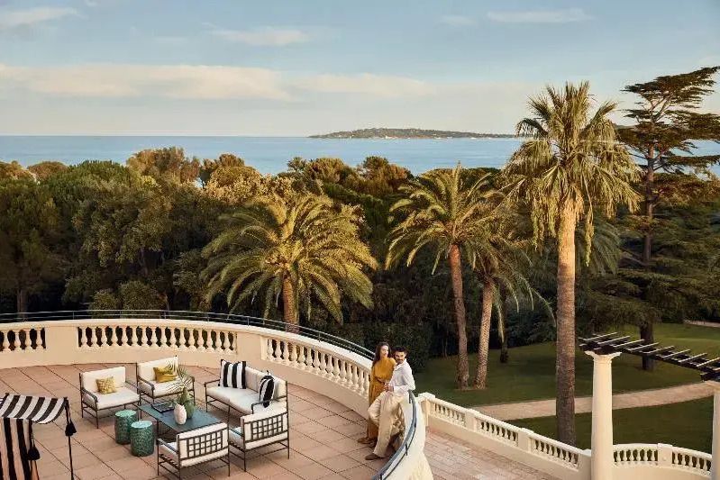 Terrasse mit Loungemöbeln und Blick auf das Meer und Palmen im Hotel Le Beauvallon