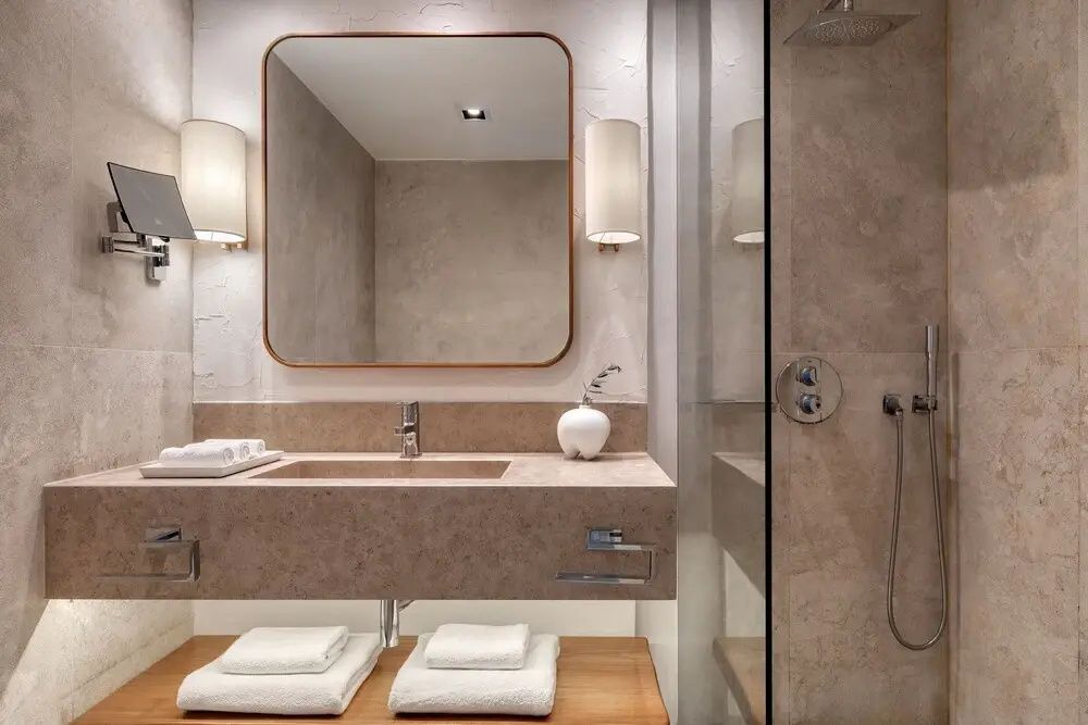 Luxuriöses Badezimmer aus Naturstein mit einem modernen Waschtisch und großer Spiegelfläche.
