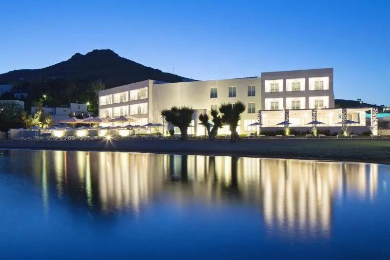 Beleuchtetes Patmos Aktis Resort bei Dämmerung direkt am Meer mit Spiegelung im ruhigen Wasser.