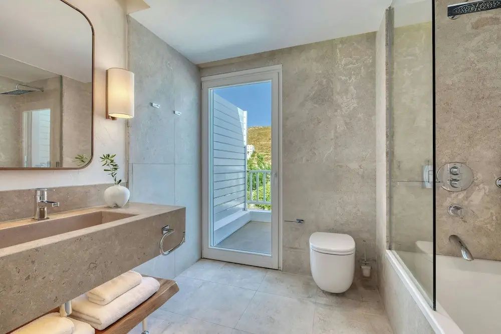 Stilvolles Badezimmer aus Naturstein mit Zugang zum Balkon im Grand Doppelzimmer des Patmos Aktis.