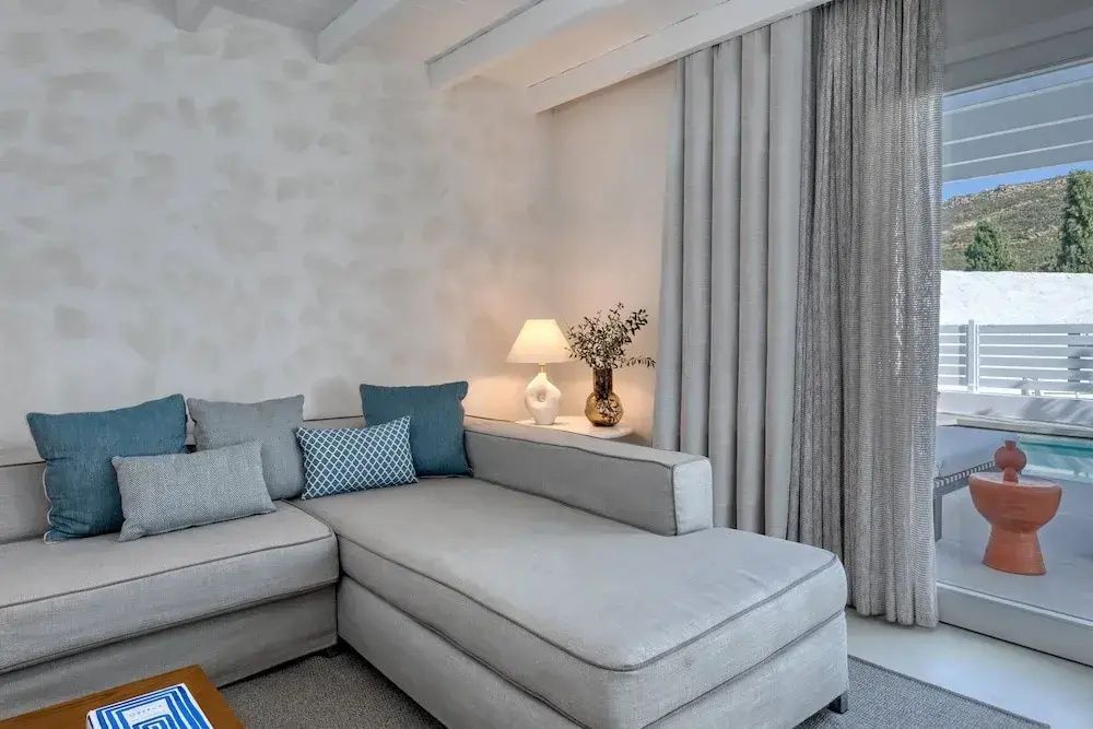 Gemütliche Sitzecke mit grauem Ecksofa, blauen Kissen und stilvoller Tischlampe im Doppelzimmer.