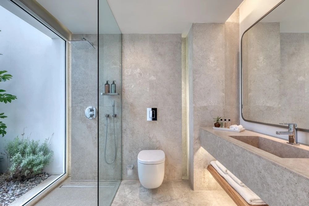Luxuriöses Badezimmer aus Naturstein mit begehbarer Glasdusche und Waschtisch im Patmos Aktis Resort.