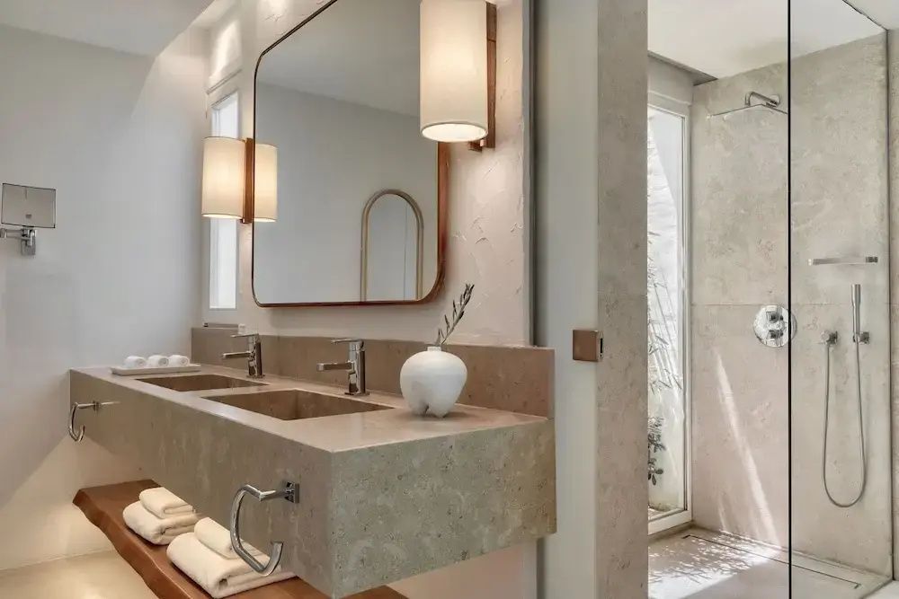 Luxuriöses Badezimmer mit Doppelwaschbecken aus Naturstein und beleuchtetem Spiegel.