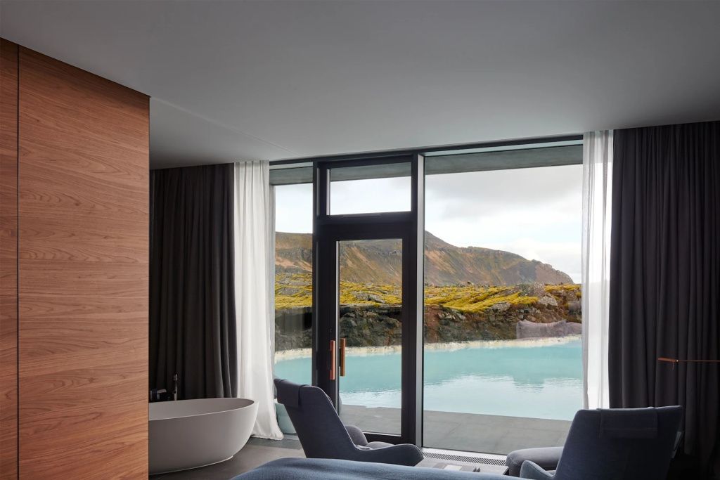 Freistehende Badewanne am Panoramafenster mit Blick auf die blaue Lagune und Felsen.