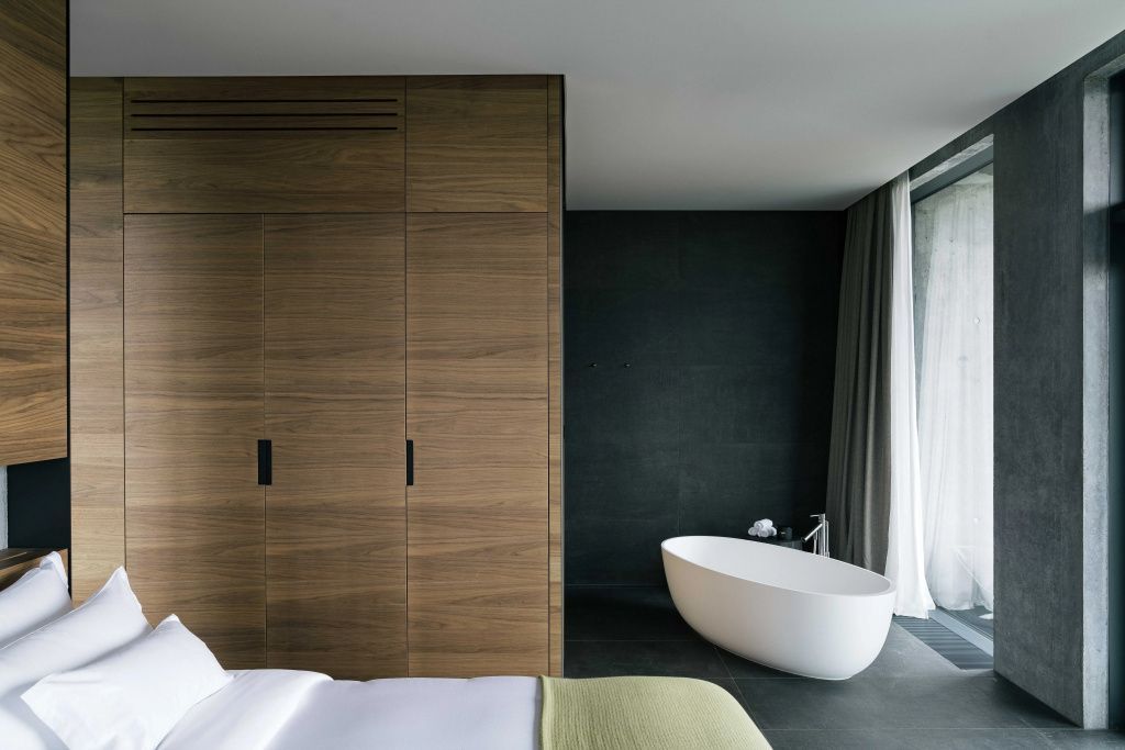 Freistehende Badewanne und eleganter Holzschrank in der dunklen Naturstein-Atmosphäre der Moss Suite.