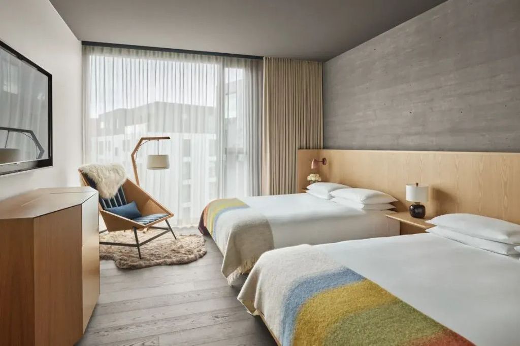 Modernes Schlafzimmer mit zwei Doppelbetten, Sessel aus Holz und bodentiefem Fenster im The Reykjavik Edition.