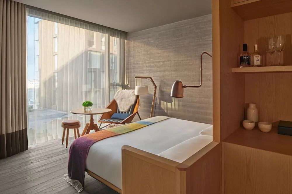Modernes Doppelzimmer im Reykjavik Edition mit Doppelbett, Sessel und Blick auf den Innenhof.
