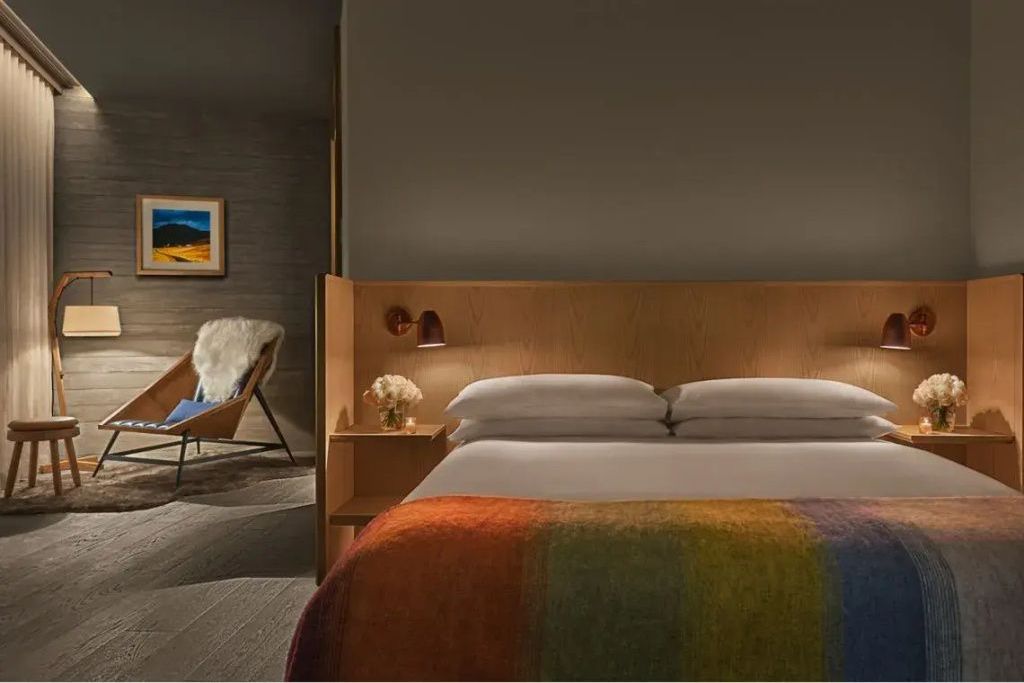 Doppelbett im Loft Zimmer mit Holzkopfteil, buntem Deckenakzent und gemütlichem Sessel im Hintergrund.