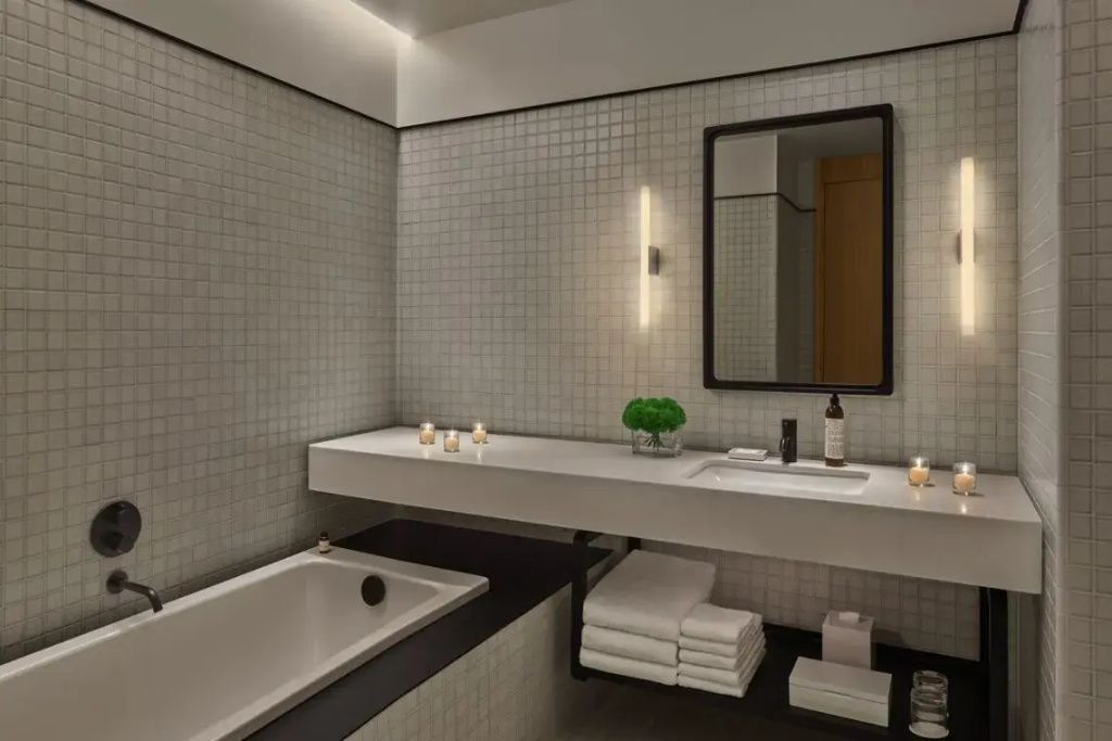 Modernes Badezimmer mit weißem Mosaik, Badewanne, Waschtisch und edlem schwarzem Spiegel.