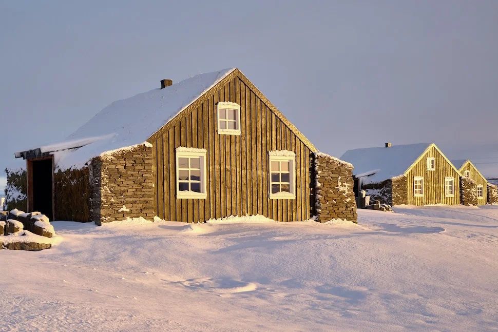 Verschneite traditionelle Hütte im Torfhús Retreat mit Natursteinmauer und Holzfassade.