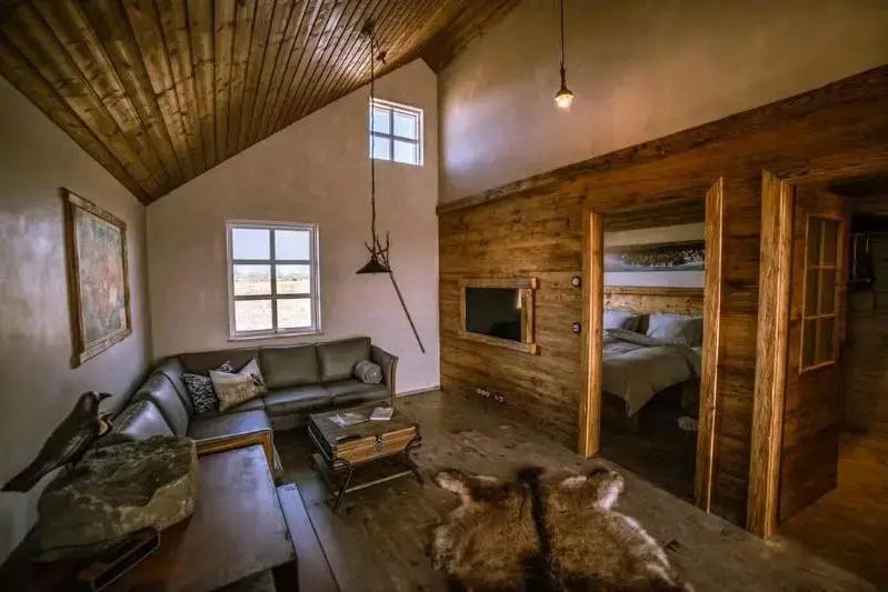 Rustikales Wohnzimmer im Torfhús Retreat mit Ledersofa, Holzverkleidung und Blick ins Schlafzimmer.