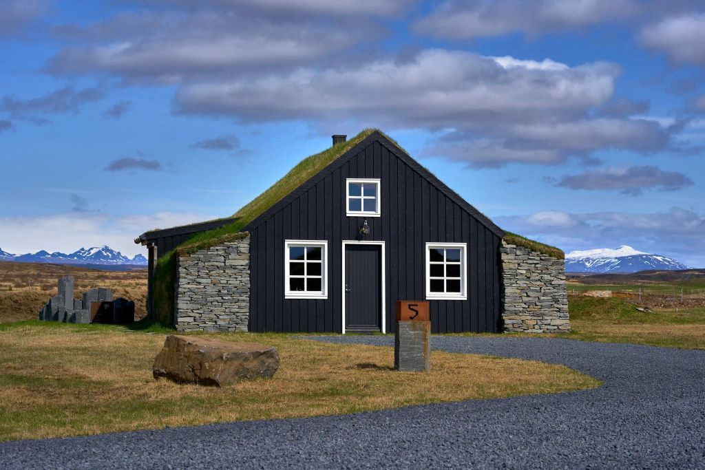 Traditionelles Torfhaus aus schwarzem Holz mit Grasdach und Natursteinmauern.