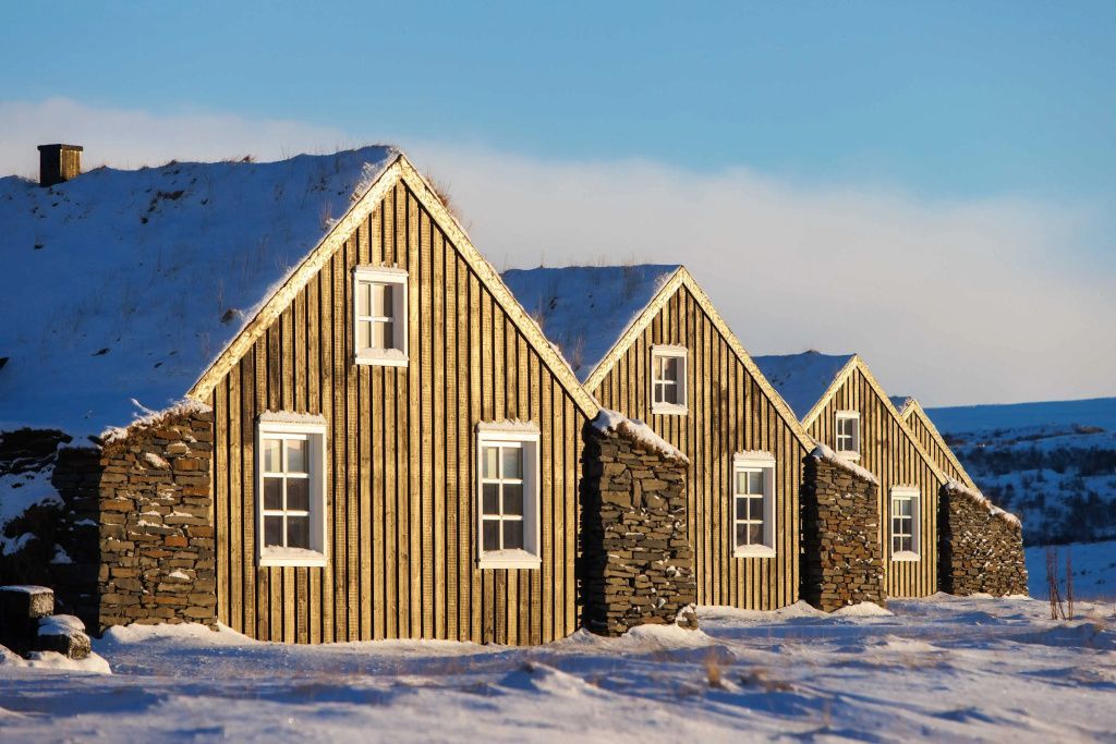 Isländische Torfhäuser im Winterkleid mit schneebedeckten Dächern und Holzfassade.
