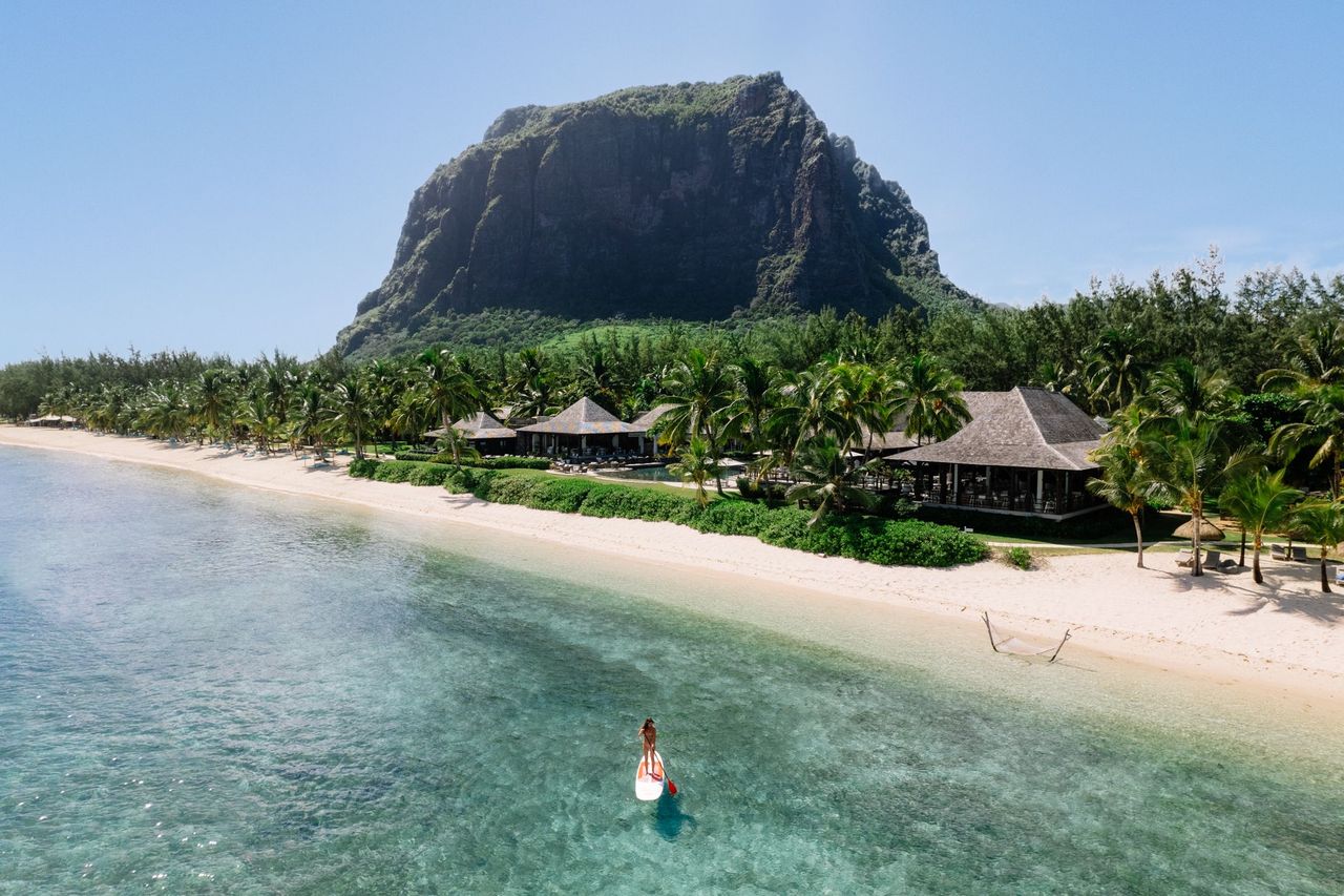 Strand am Fuß des Le Morne Brabant im Südwesten von Mauritius, davor eine Stand-up-Paddlerin in der Lagune