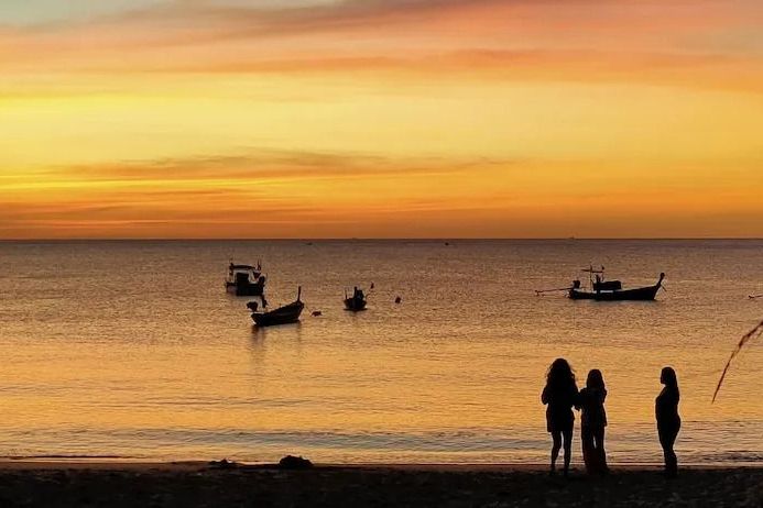 Sonnenuntergang am Strand mit Booten und zwei Silhouetten