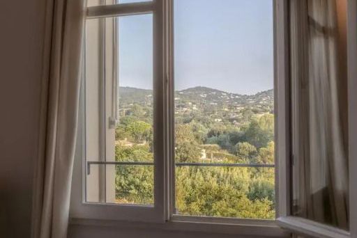 Blick aus dem Fenster mit Aussicht auf grüne Hügel und blauen Himmel