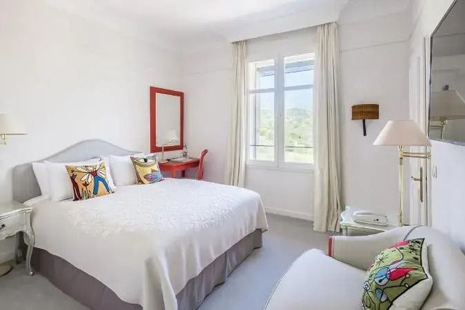 Helles Hotelzimmer mit Doppelbett, Fenster und rotem Schreibtisch