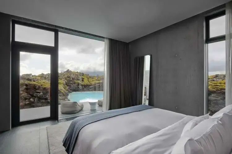 Modernes Schlafzimmer der Blue Lagoon Suite mit direktem Blick auf die blaue Lagune und Vulkanlandschaft.