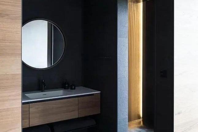 Stilvolles Badezimmer mit Waschtisch, rundem Spiegel und Regendusche in der Lava Junior-Suite