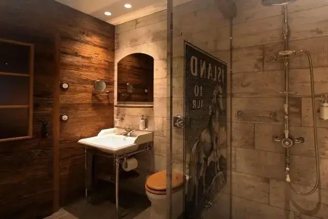 Badezimmer im Torfhús Retreat mit Holz und Steinwand, Waschbecken und Dusche.