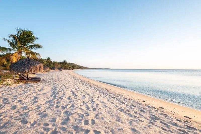 Weißer Sandstrand mit klarem blauem Wasser bei Sonnenuntergang