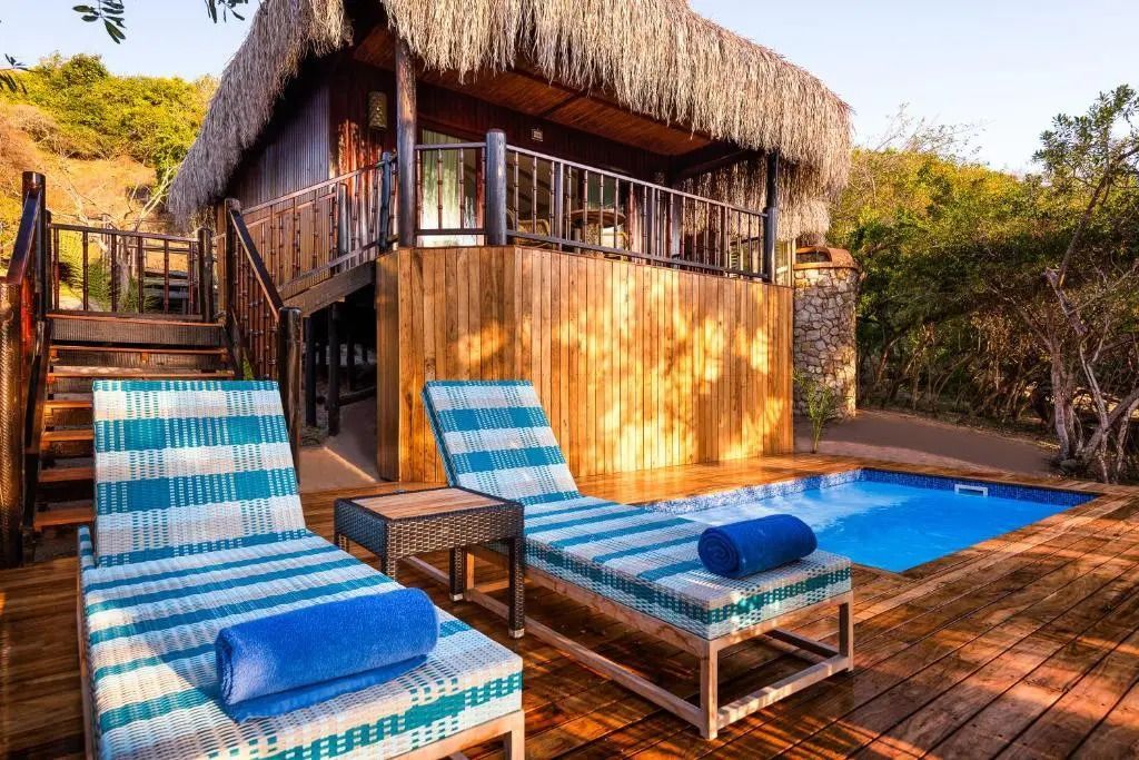 Villa mit Reetdach und privatem Pool, umgeben von tropischer Vegetation.