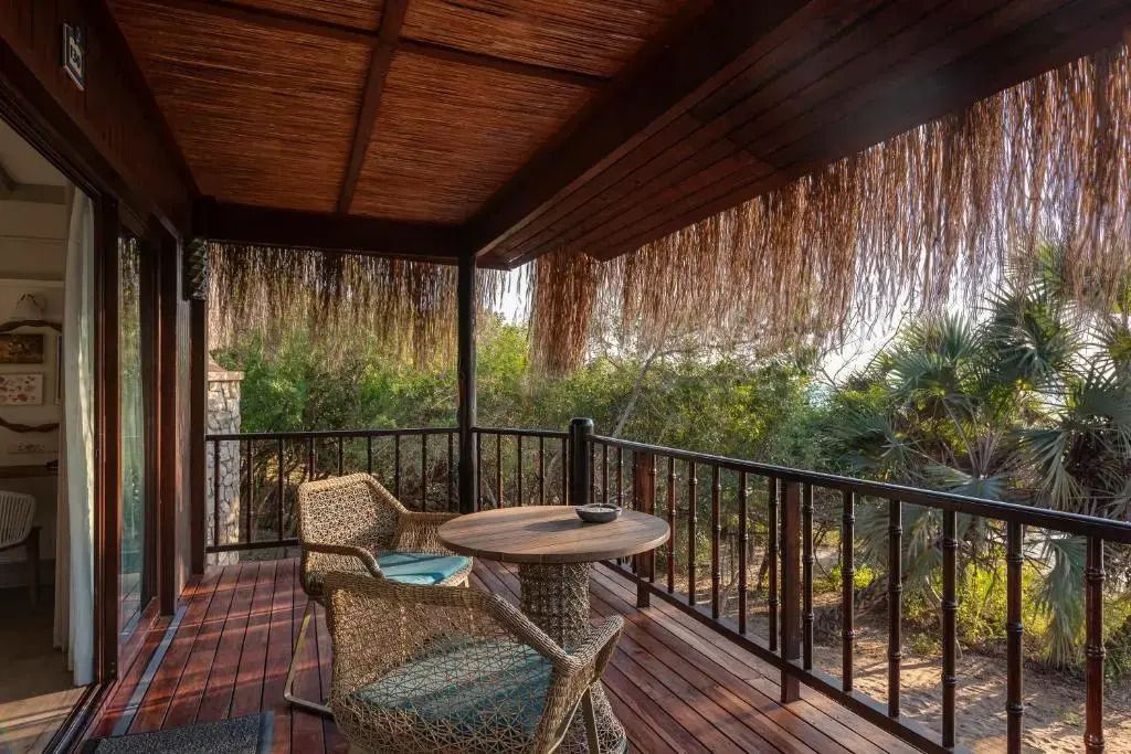 Balkon mit Strohüberdachung und Blick auf tropische Vegetation.