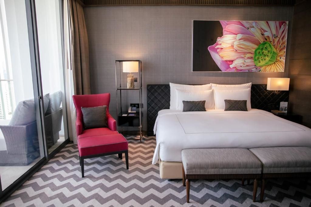 Luxuriöse Sukhothai Suite mit Doppelbett, rotem Sessel und moderner Beleuchtung.