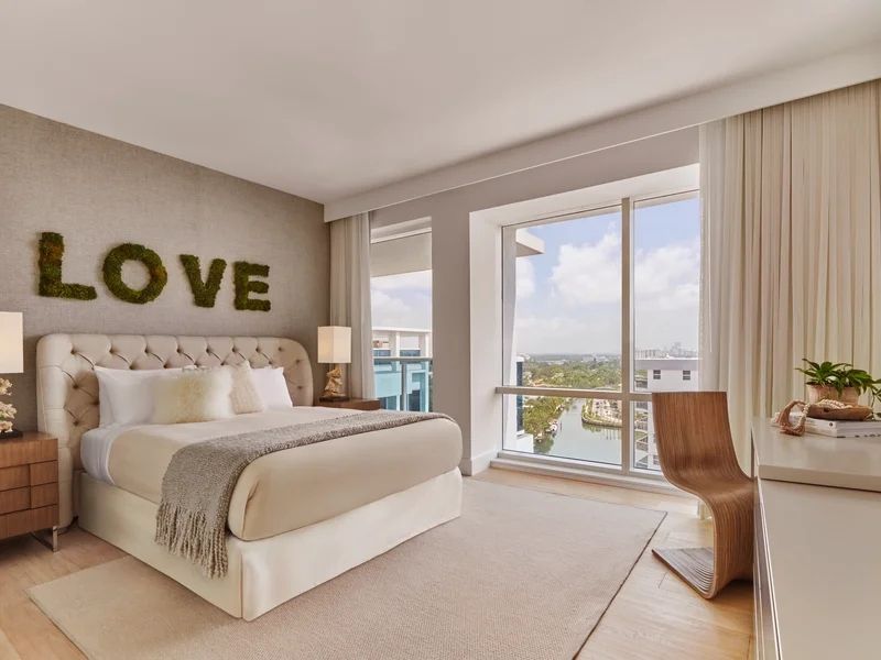 Modernes Schlafzimmer mit großem Fenster und Blick auf Wasser und Skyline.