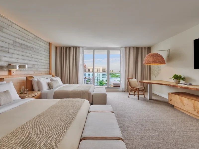Zimmer mit zwei Betten, großer Fensterfront und Blick auf die Stadt.