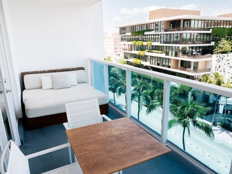Balkon mit Sitzgelegenheit und Aussicht auf grüne Palmen und moderne Gebäude.