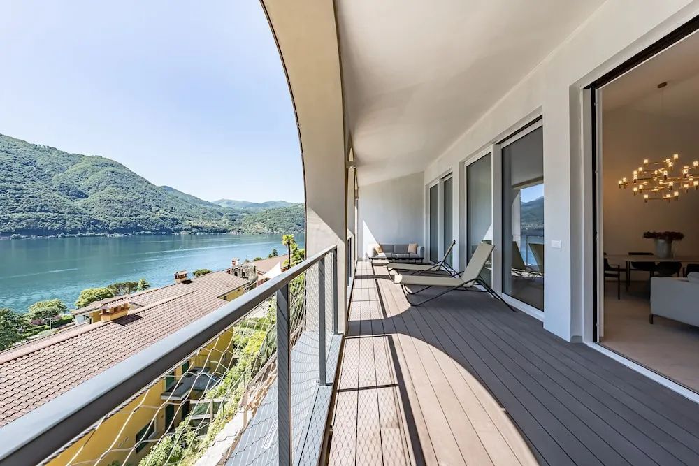 Überdachter Balkon mit Liegestühlen und freiem Blick auf den See und die umliegenden Berge.