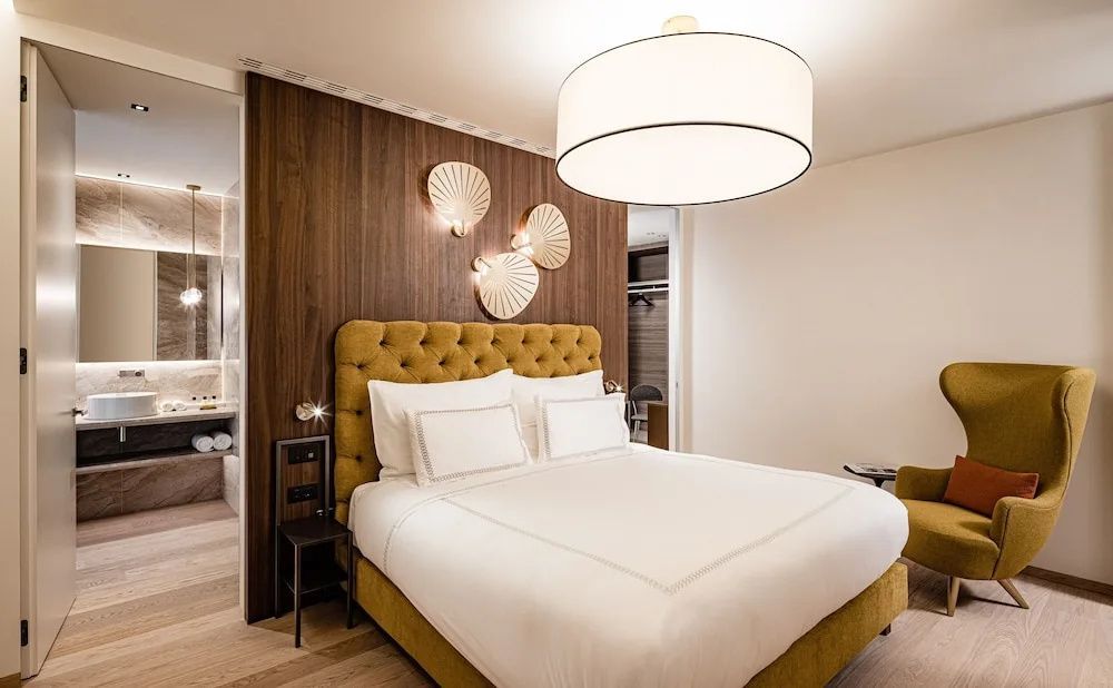 Doppelbett mit gelbem gepolstertem Kopfteil vor Holzwandverkleidung im Hotelzimmer