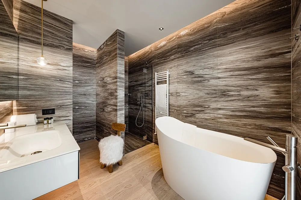 Freistehende weiße Badewanne in einem Bad mit dunkel gemusterten Steinwänden.