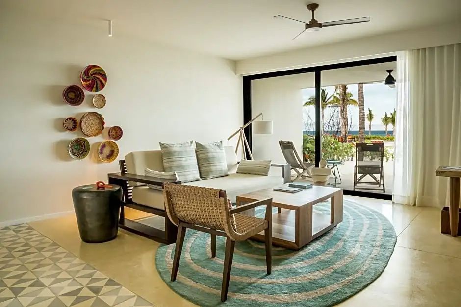 Wohnbereich einer Hotelunterkunft mit Sofa, Sessel, Couchtisch und Blick auf die Außenterrasse.