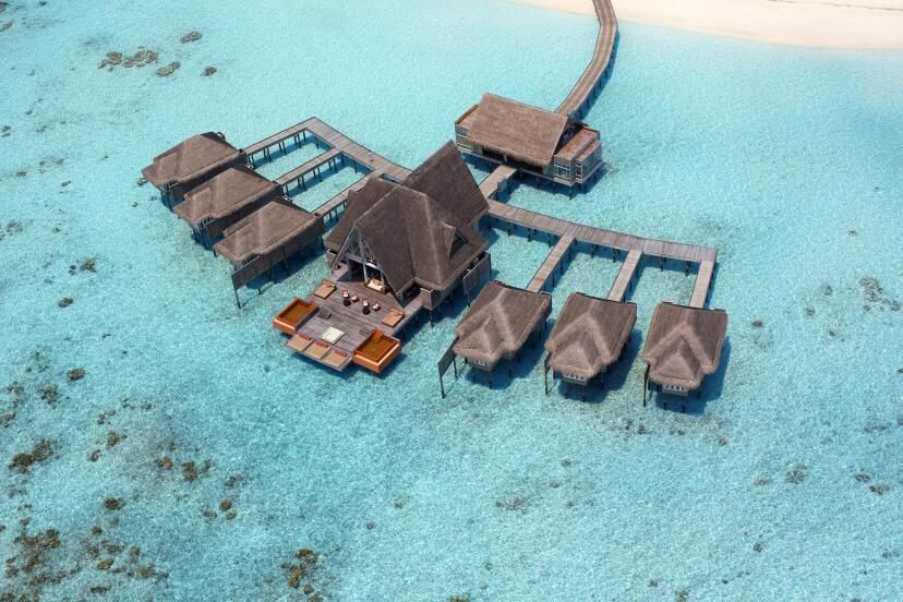 Luftaufnahme der luxuriösen Overwater-Villen des Anantara Kihavah Maldives Villas Resorts, eingebettet in türkisblaues Wasser mit hölzernen Stegen, die zu den privaten Unterkünften führen.