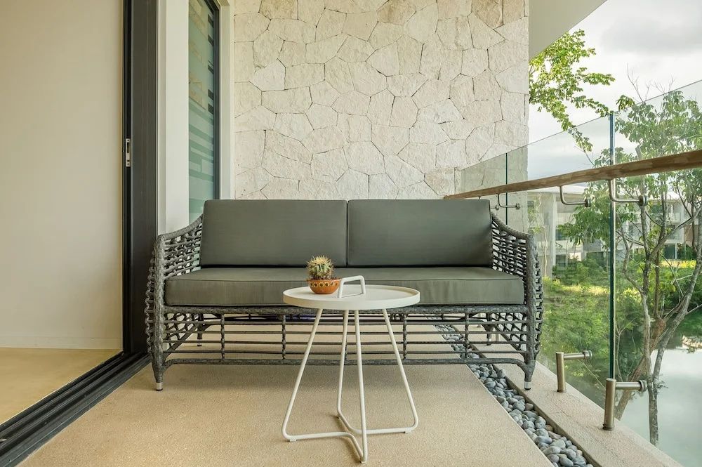 Überdachter Balkon mit grauem Geflechtsofa, kleinem Beistelltisch und Steinwand.