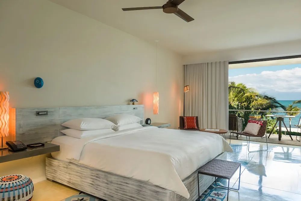 Geräumiges Hotelzimmer mit weißem Doppelbett, Deckenventilator und Zugang zum Balkon.