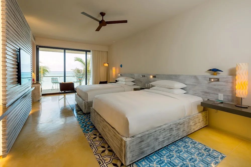 Doppelzimmer mit zwei Betten, gemusterten Fliesen und großer Fenstertür zum Balkon mit Meerblick.