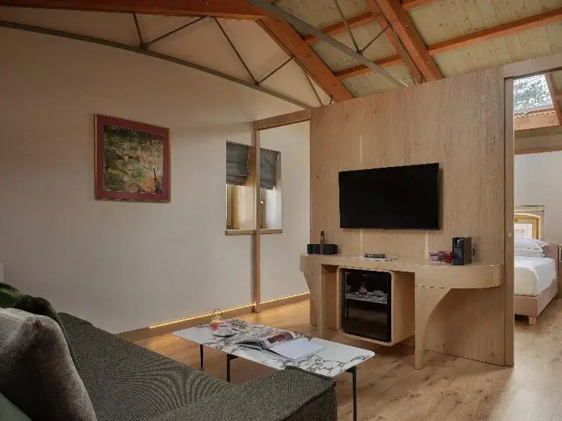 Wohnbereich eines Zimmers mit Fernseher, Sofa und Couchtisch unter Holzgebälk.
