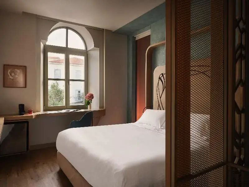Doppelbett im Hotelzimmer mit Rundbogenfenster und Blick auf die Stadt.