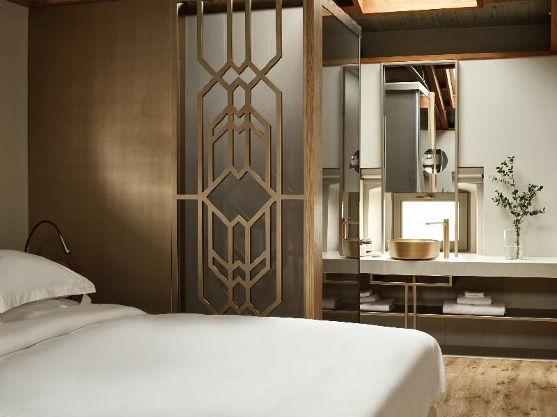 Blick vom Doppelbett auf ein goldenes Waschtischbecken hinter einer Trennwand.