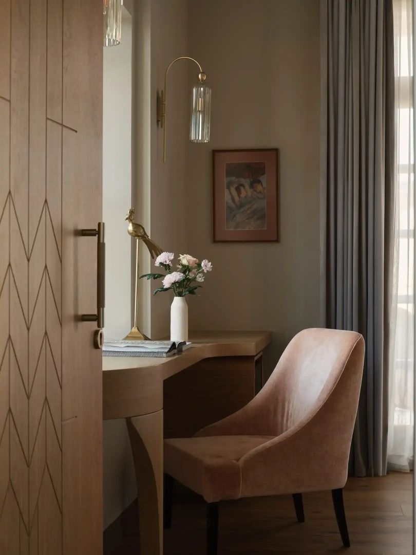 Schreibtischbereich im Hotelzimmer mit Sessel, Vase mit Blumen und Wanddekoration.