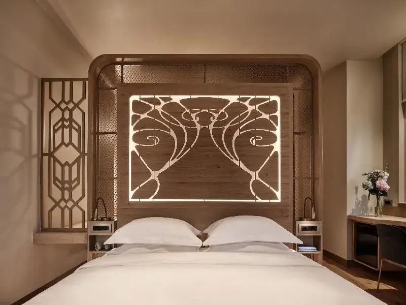 Doppelbett mit kunstvoll beleuchtetem Kopfteil aus Holz im Hotelzimmer.